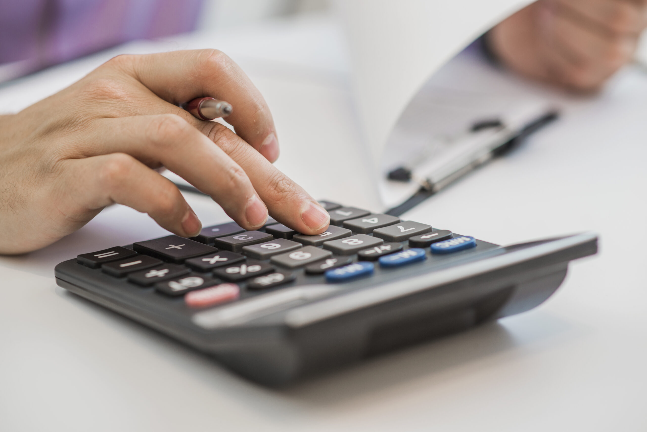 Photo of hands holding pencil and pressing calculator buttons ov Imposto de Renda